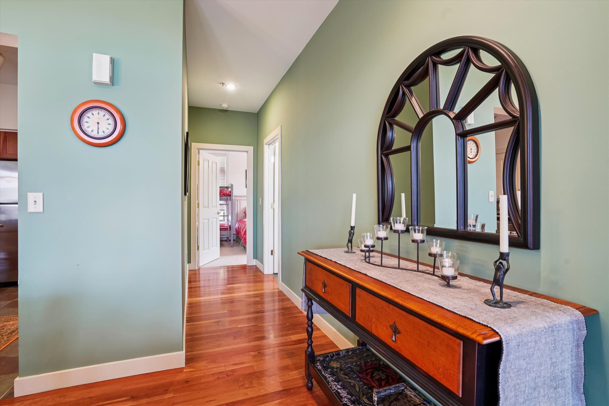 A welcoming hallway connects the main living area to the bedrooms, featuring warm wood flooring, soft lighting, and an elegant mirror detail that reflects the home's inviting atmosphere.