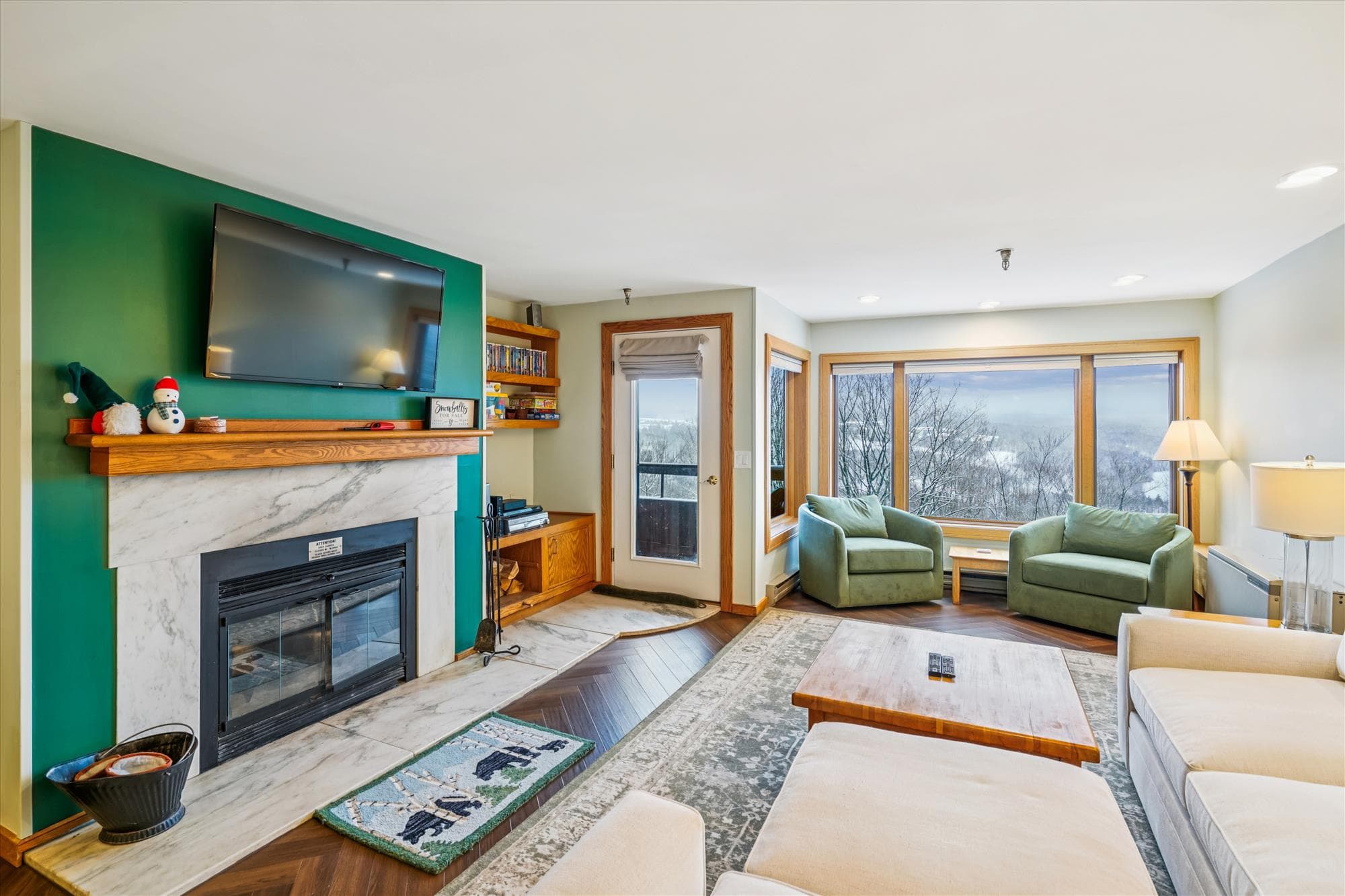 Relax in the inviting living room featuring a fireplace, large flat-screen TV, and expansive windows showcasing beautiful mountain views.