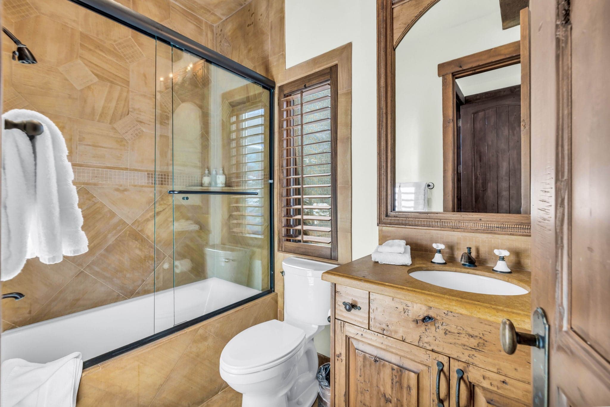 Bathroom with glass-enclosed shower, wood vanity, and rustic stone details.