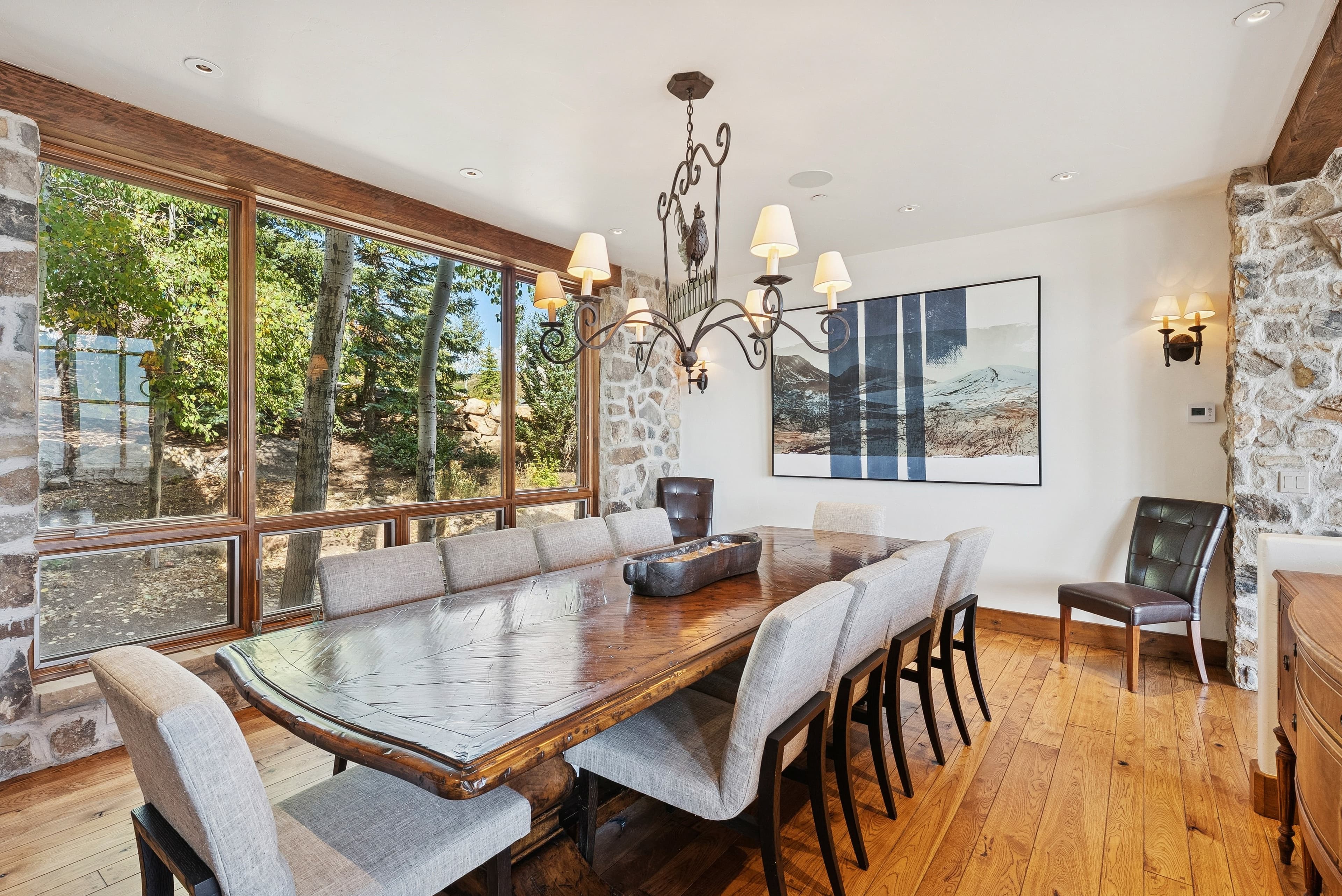 Formal dining room with long wooden table, chandelier, and large windows with forest views.