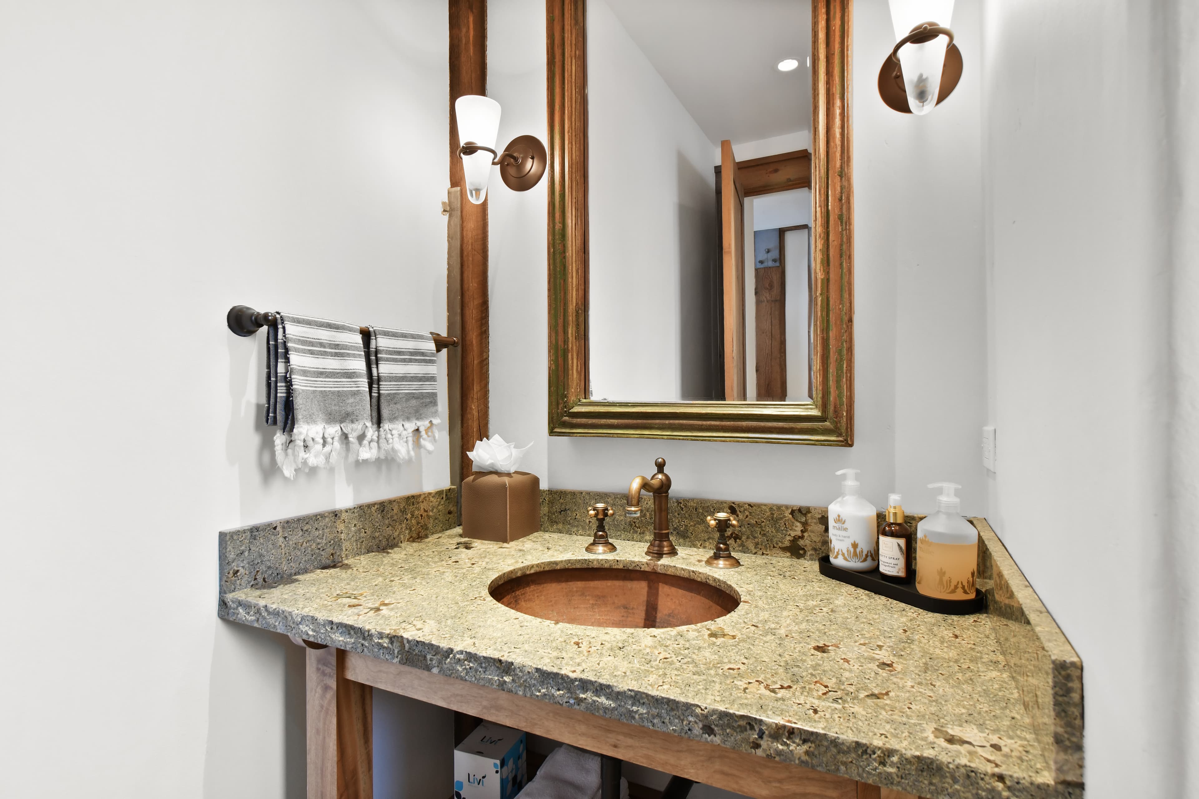 A granite countertop with a sink and soaps in front of a bathroom mirror.