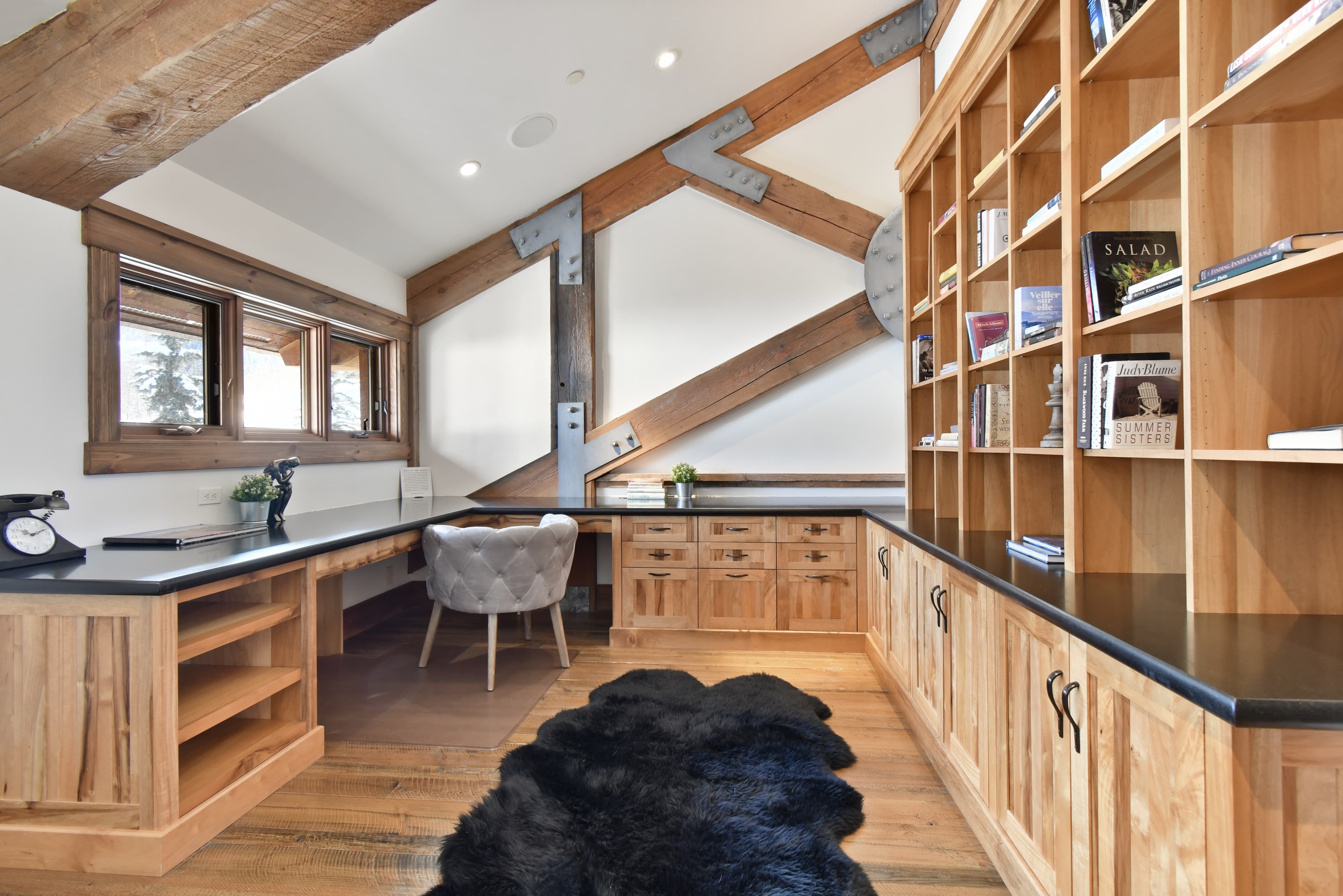 High windows shine light into a private office space with large wooden bookshelves and a simple chair tucked into a desk.