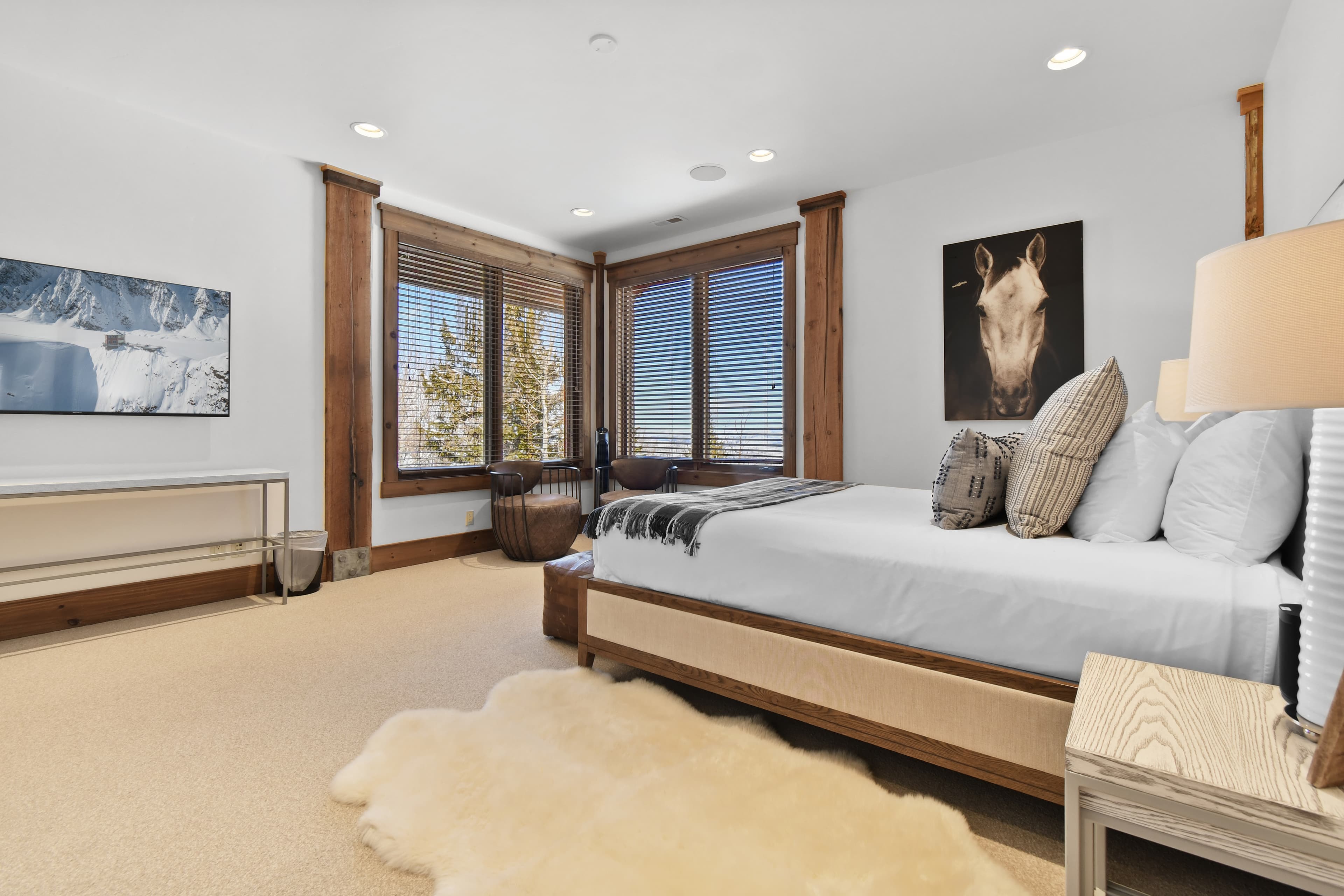 Two windows form the corner of a bedroom, in front of a large white bed.