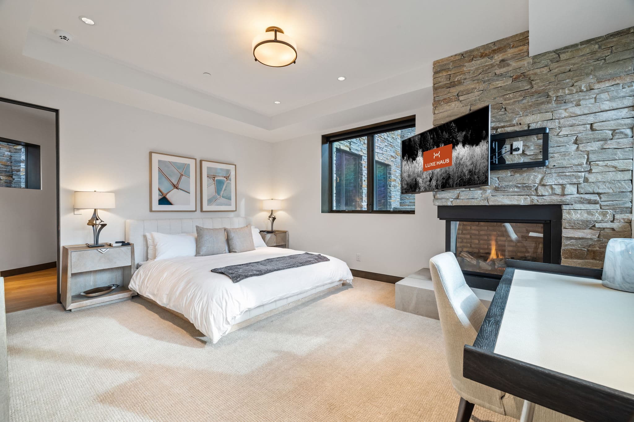 A bedroom with a bed, a desk, and a fireplace.